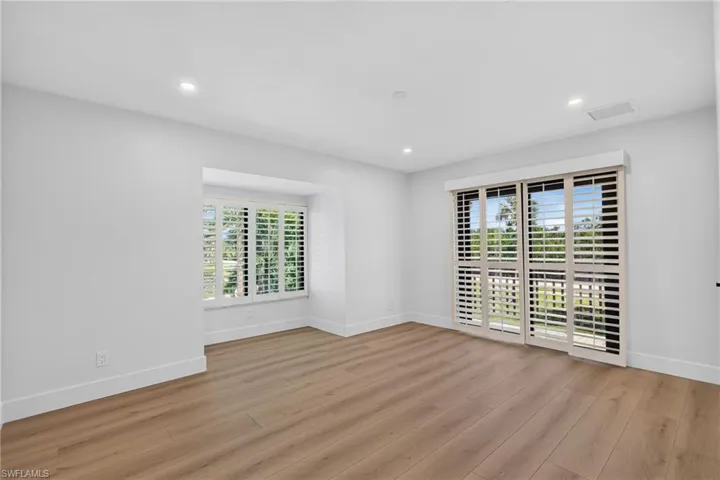 Primary Bedroom featuring wood-finish flooring, recessed lighting, a recessed window area with plantation shutters, and sliding glass doors with integrated plantation shutters