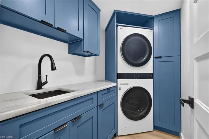 Blue cabinetry featuring matte black hardware, stone-surface countertop, under-mount sink with a high-arch pull-down faucet, and custom-built integrated laundry enclosure