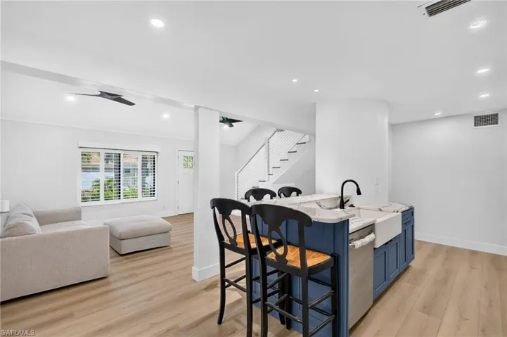 Kitchen island featuring a farmhouse-style apron sink, stone-finish countertop, and matte black faucet, complemented by wood-finish flooring, recessed lighting, and a staircase with horizontal cable railing