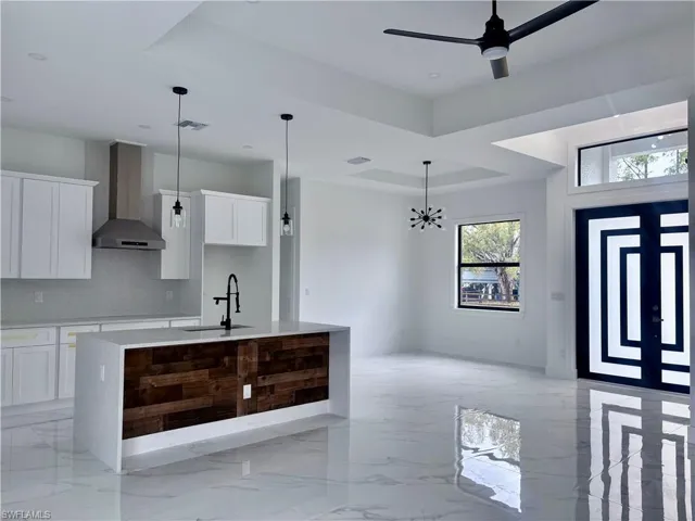 Kitchen featuring an island with sink, white cabinetry, and wall chimney range hood