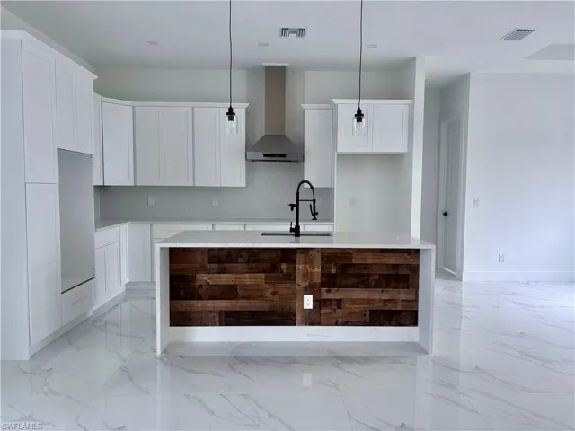 Kitchen featuring a center island with sink, decorative light fixtures, wall chimney range hood, and sink