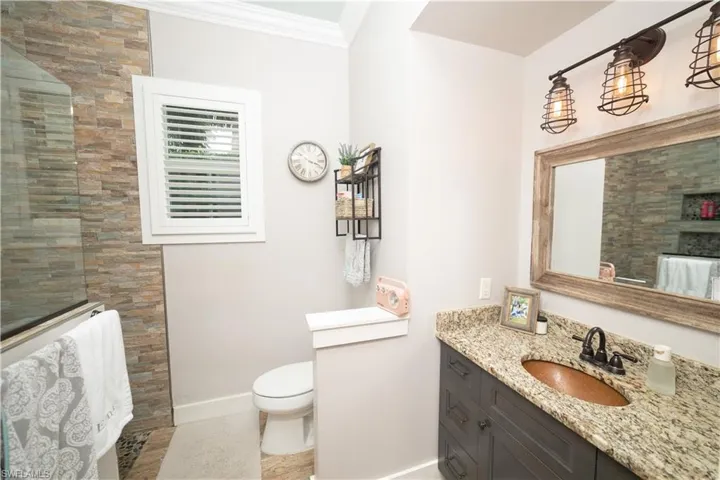 Bathroom with crown molding, vanity, baseboards, a tile shower, and toilet