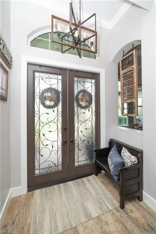 Foyer entrance with french doors, wood finished floors, baseboards, and an inviting chandelier