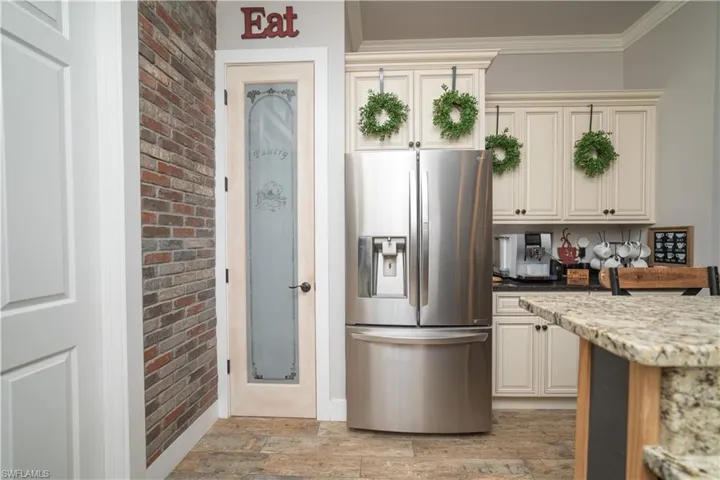 Kitchen with crown molding, stainless steel fridge with ice dispenser, light wood finished floors, cream cabinetry, and light stone countertops