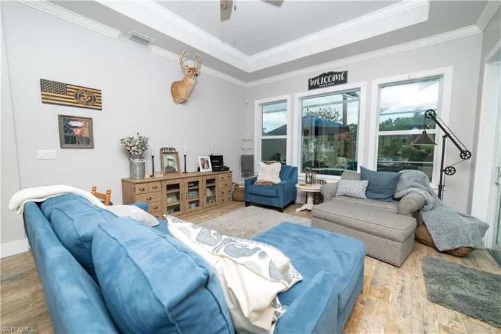 Living room featuring wood finished floors, visible vents, a ceiling fan, ornamental molding, and baseboards