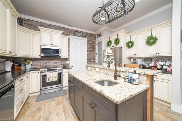 Kitchen with cream cabinetry, a sink, light wood-type flooring, gray cabinetry, and appliances with stainless steel finishes
