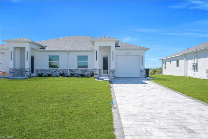 Prairie-style home with stucco siding, stone siding, a front yard, an attached garage, and decorative driveway