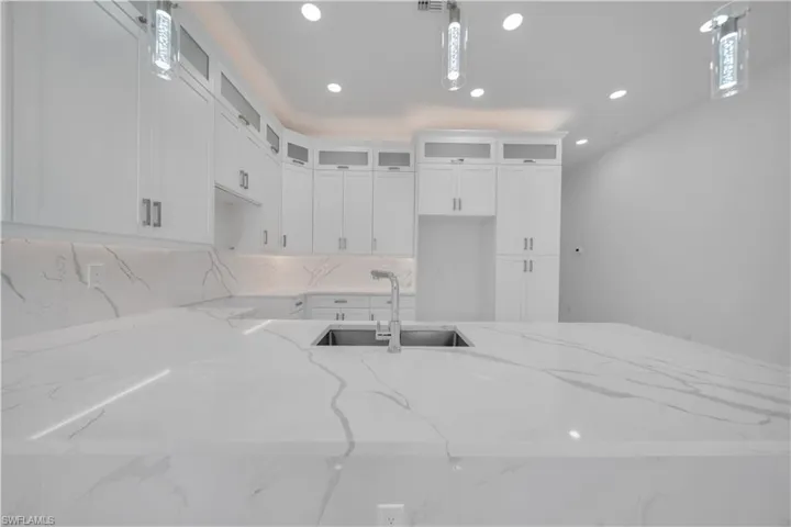 Kitchen featuring white cabinets, pendant lighting, light stone counters, and glass fronted cabinets