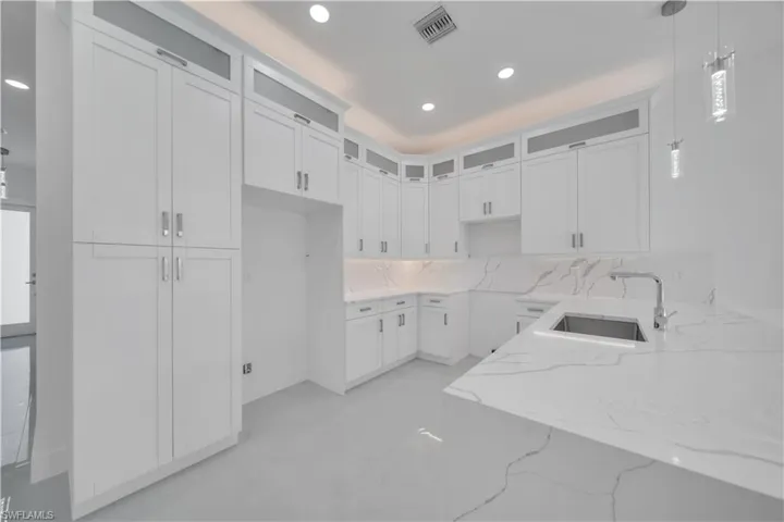 Kitchen featuring white cabinets, light stone countertops, glass insert cabinets, and decorative light fixtures