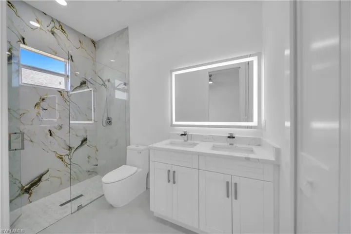 Full bath featuring double vanity and a marble finish shower