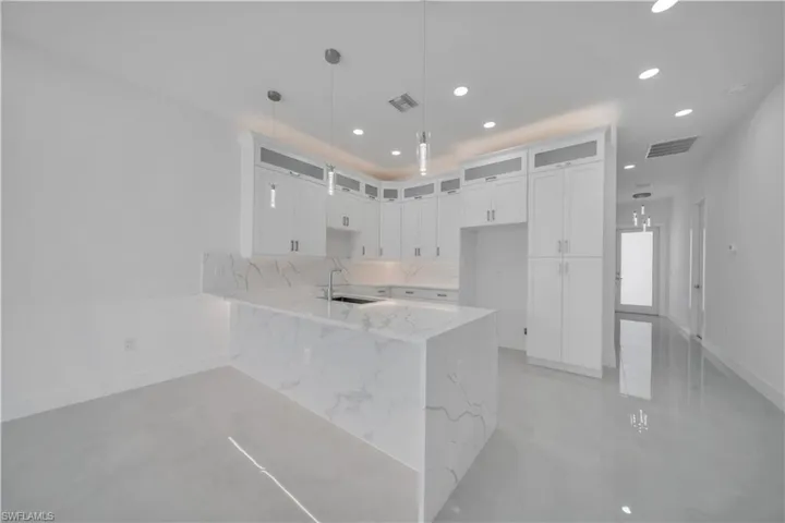Kitchen with light stone counters, glass insert cabinets, white cabinets, a peninsula, and pendant lighting