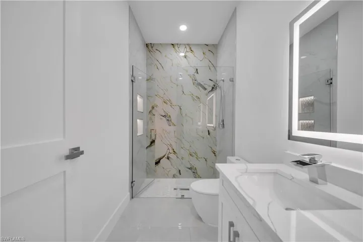 Bathroom with a marble finish shower, vanity, and recessed lighting