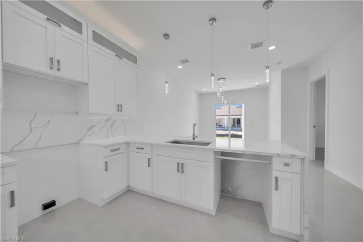 Kitchen featuring white cabinets, light stone counters, hanging light fixtures, and a peninsula