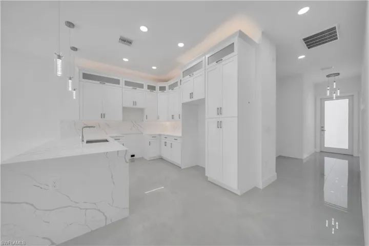 Kitchen with hanging light fixtures, light stone countertops, white cabinets, glass insert cabinets, and tasteful backsplash