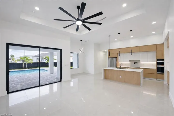 Dual tone kitchen featuring open floor plan, a large island with sink, modern cabinets, decorative light fixtures, and a raised ceiling