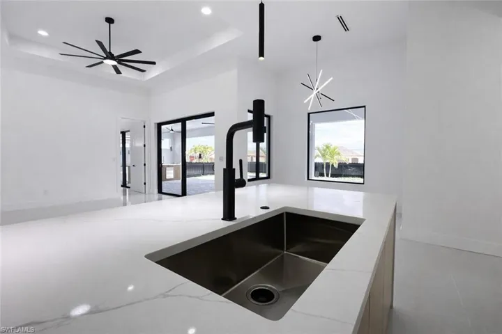 Kitchen featuring light stone counters, a tray ceiling, open floor plan, and hanging light fixtures