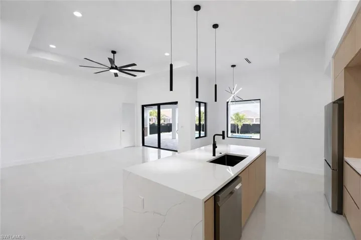 Kitchen with modern cabinets, a kitchen island with sink, stainless steel appliances, light stone countertops, and suspended lighting