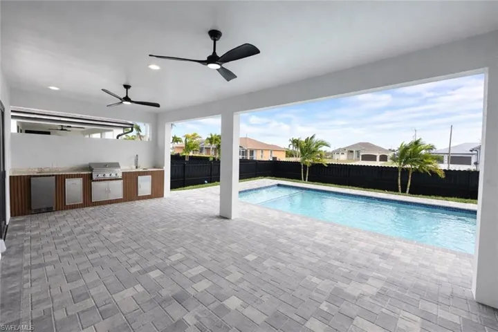 View of swimming pool with an outdoor kitchen, patio surround, a fenced backyard, and a residential view