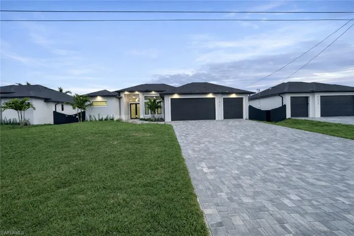 Prairie-style home with a front yard, stucco siding, decorative driveway, and an attached garage