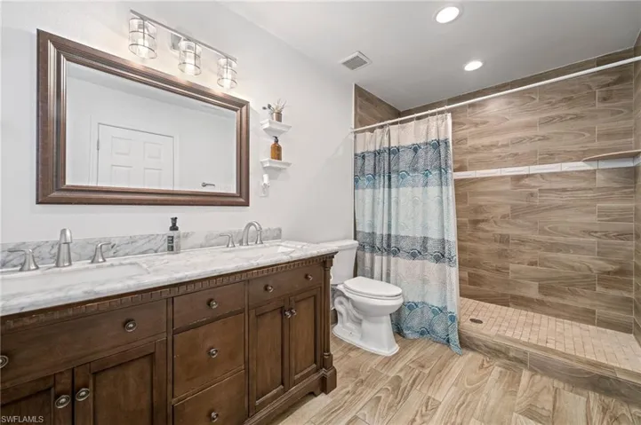 Full bath featuring a tile shower, double vanity, recessed lighting, and wood finished floors