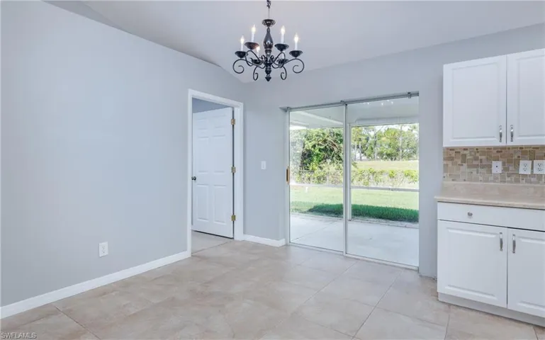 Unfurnished dining area with a notable chandelier, light tile patterned flooring, and vaulted ceiling