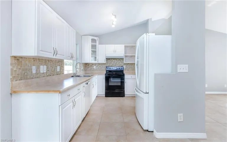 Kitchen with vaulted ceiling, sink, light tile patterned flooring, white cabinetry, and white appliances