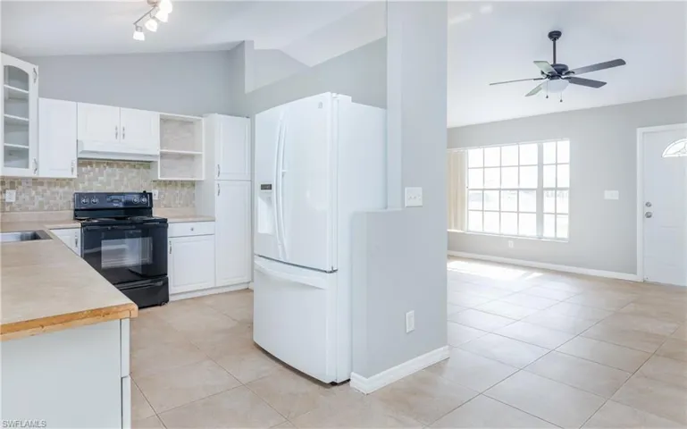 Kitchen featuring white cabinetry, white fridge with ice dispenser, vaulted ceiling, and black range with electric stovetop