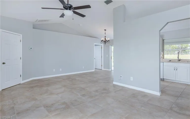 Tiled spare room featuring sink, vaulted ceiling, and ceiling fan with notable chandelier