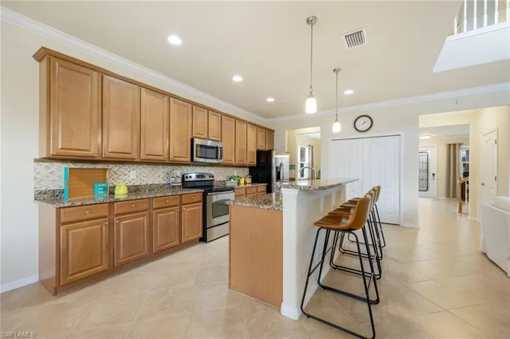 Kitchen with backsplash, light stone countertops, an island with sink, appliances with stainless steel finishes, and decorative light fixtures