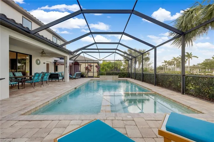 View of pool with glass enclosure, ceiling fan, and a patio area
