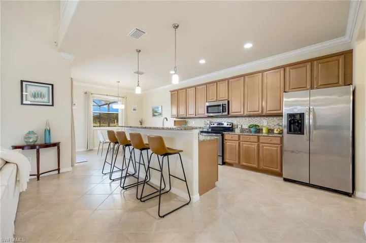 Kitchen featuring light stone countertops, stainless steel appliances, crown molding, decorative light fixtures, and a kitchen island