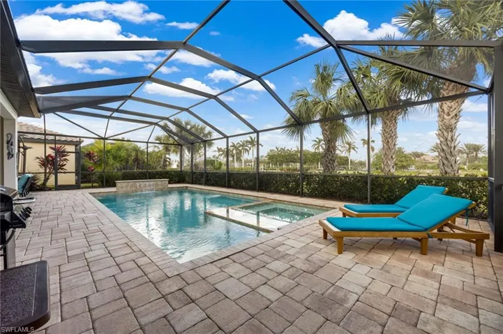 View of swimming pool with glass enclosure, a patio area, and an in ground hot tub