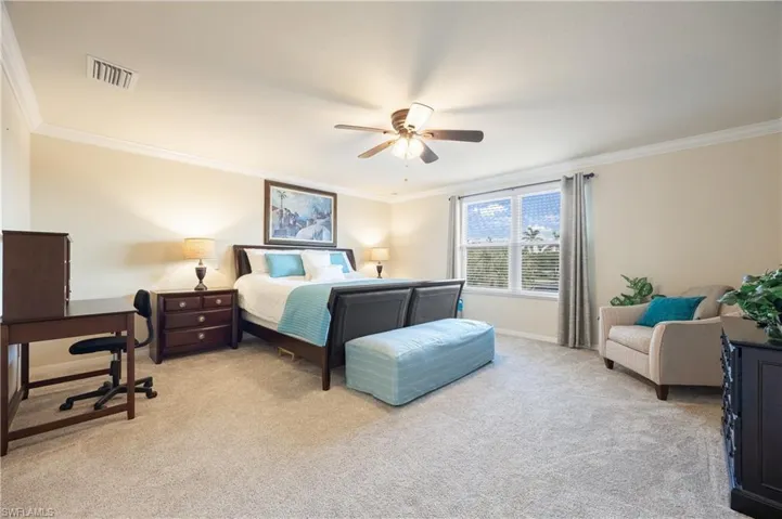 Carpeted bedroom with ceiling fan and crown molding