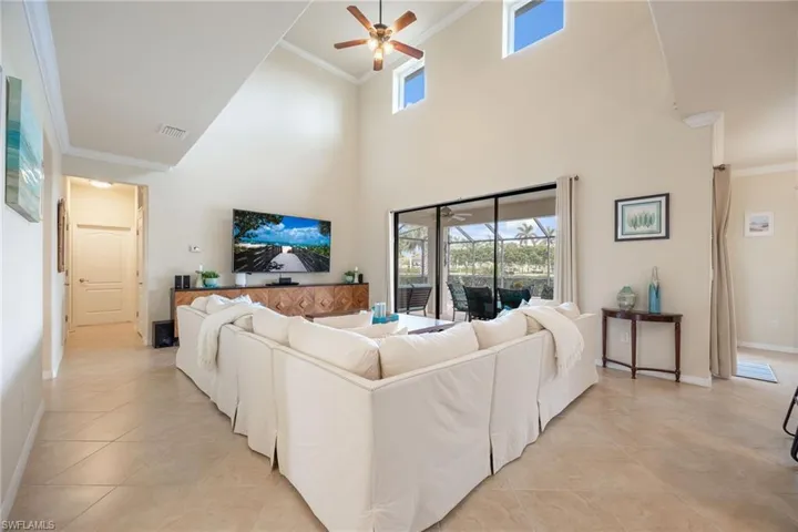 Tiled living room with a towering ceiling, ceiling fan, and crown molding