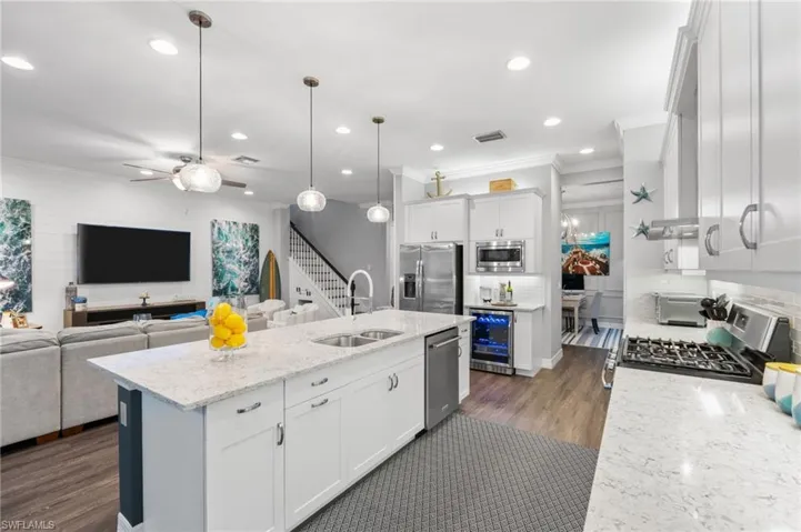 Kitchen featuring appliances with stainless steel finishes, dark hardwood / wood-style flooring, white cabinetry, wine cooler, and a kitchen island with sink