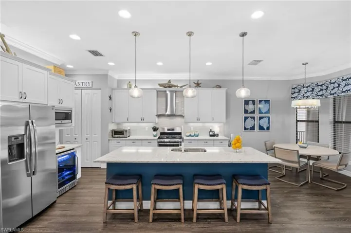 Kitchen with an island with sink, stainless steel appliances, wall chimney exhaust hood, and white cabinets