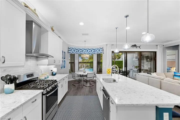Kitchen with sink, appliances with stainless steel finishes, wall chimney exhaust hood, and decorative light fixtures