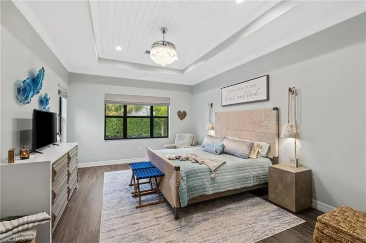 Bedroom with ornamental molding, an inviting chandelier, dark hardwood / wood-style floors, and a tray ceiling