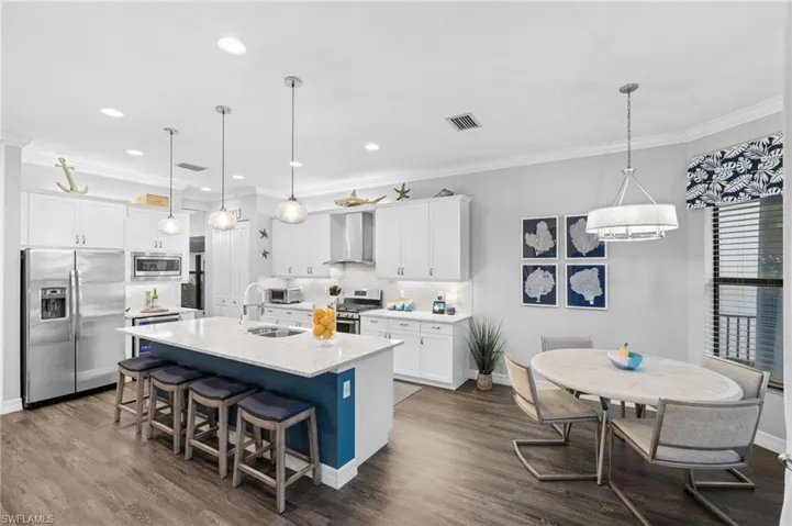 Kitchen featuring appliances with stainless steel finishes, wall chimney range hood, dark hardwood / wood-style floors, a breakfast bar area, and a center island with sink