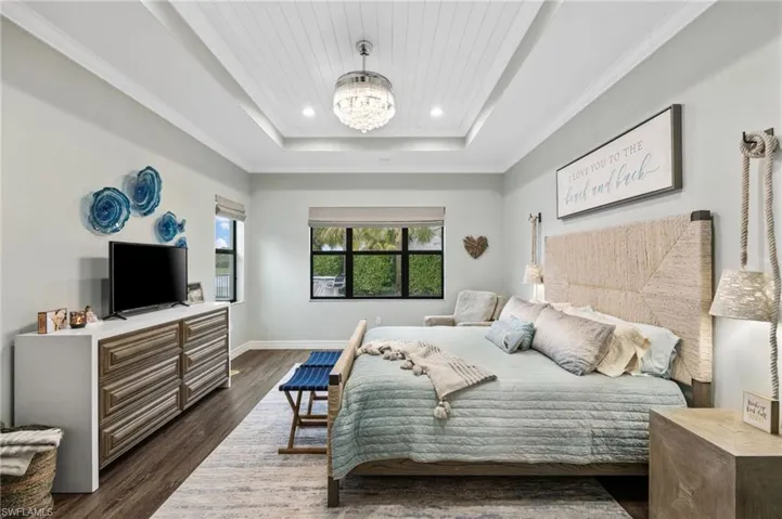 Bedroom featuring ornamental molding, a raised ceiling, dark hardwood / wood-style floors, and a notable chandelier
