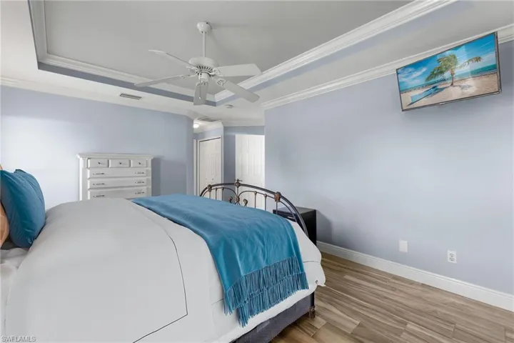 Bedroom featuring a closet, ceiling fan, a tray ceiling, ornamental molding, and wood-type flooring