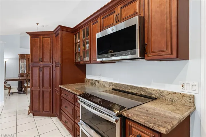 Kitchen with light stone countertops, ornamental molding, light tile floors, and stainless steel appliances