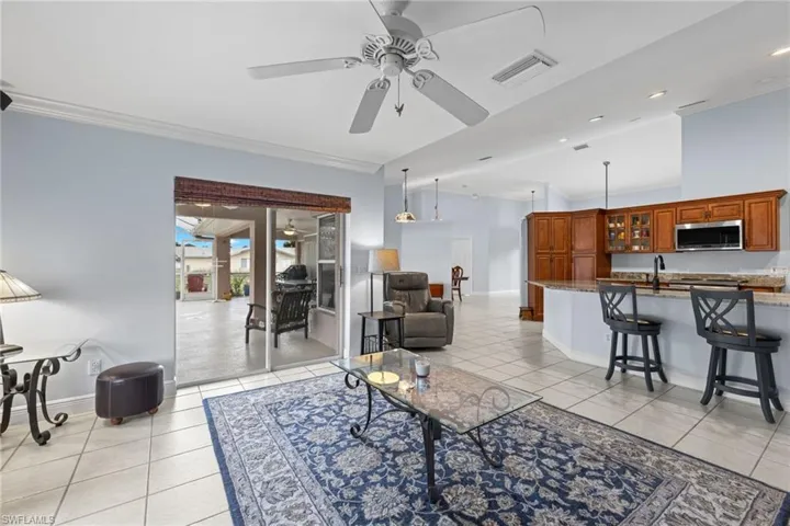 Living room featuring sink, ceiling fan, light tile flooring, and crown molding