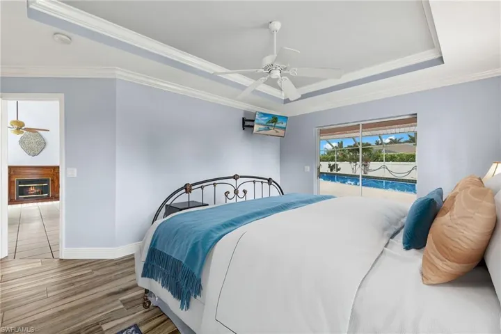 Bedroom with ornamental molding, hardwood / wood-style flooring, access to exterior, ceiling fan, and a raised ceiling