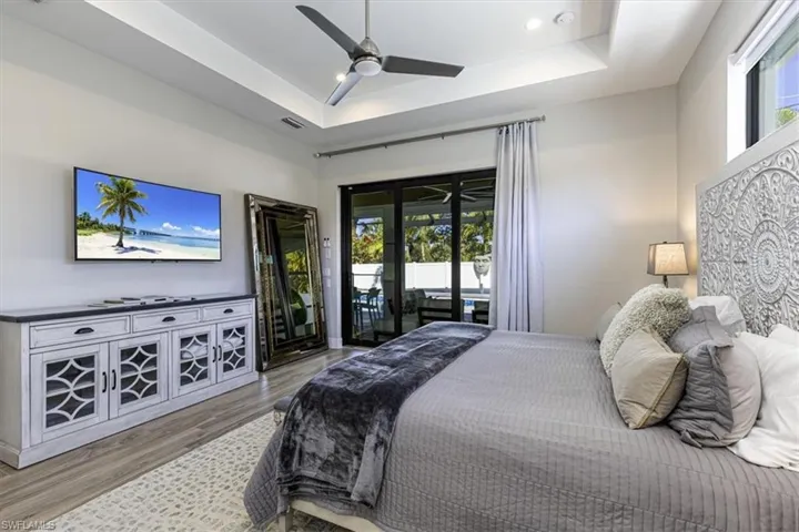 Bedroom featuring access to exterior, ceiling fan, a tray ceiling, wood finished floors, and recessed lighting