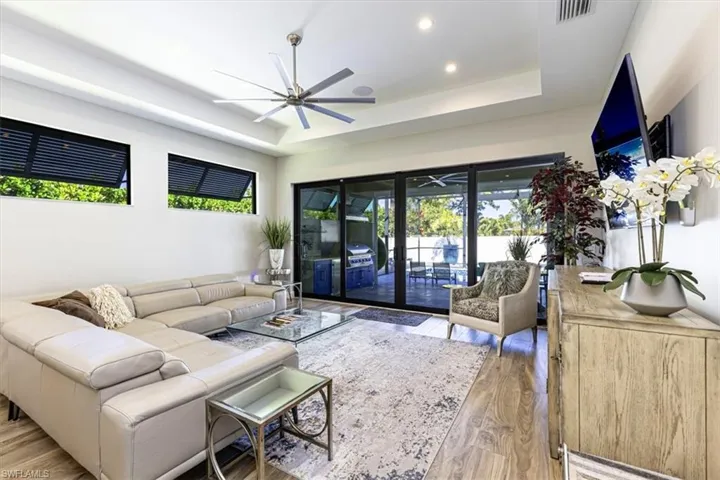 Living room with light wood-style floors, a tray ceiling, a ceiling fan, and recessed lighting