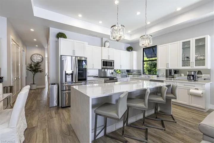 Kitchen with a raised ceiling, stainless steel appliances, decorative light fixtures, light stone counters, and white cabinets