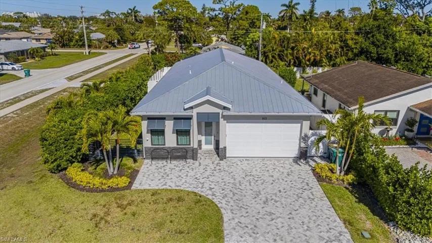 Ranch-style house featuring decorative driveway, a garage, a front lawn, a metal roof, and view of scattered trees