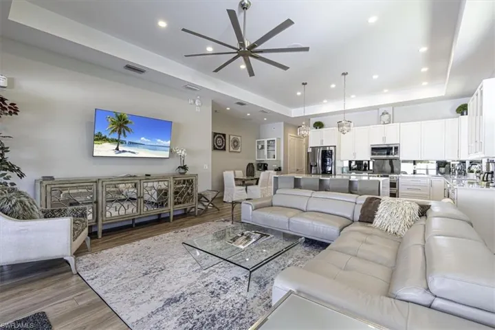 Living area with a tray ceiling, light wood-style flooring, a ceiling fan, and recessed lighting