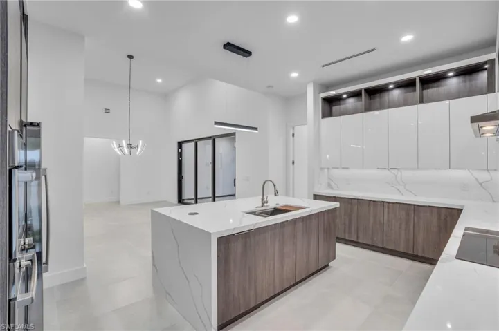 Kitchen with decorative light fixtures, a center island with sink, white cabinetry, light stone countertops, and sink